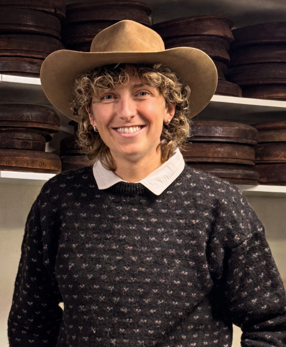 Person wearing a cowboy hat and patterned sweater in front of shelves with wooden items