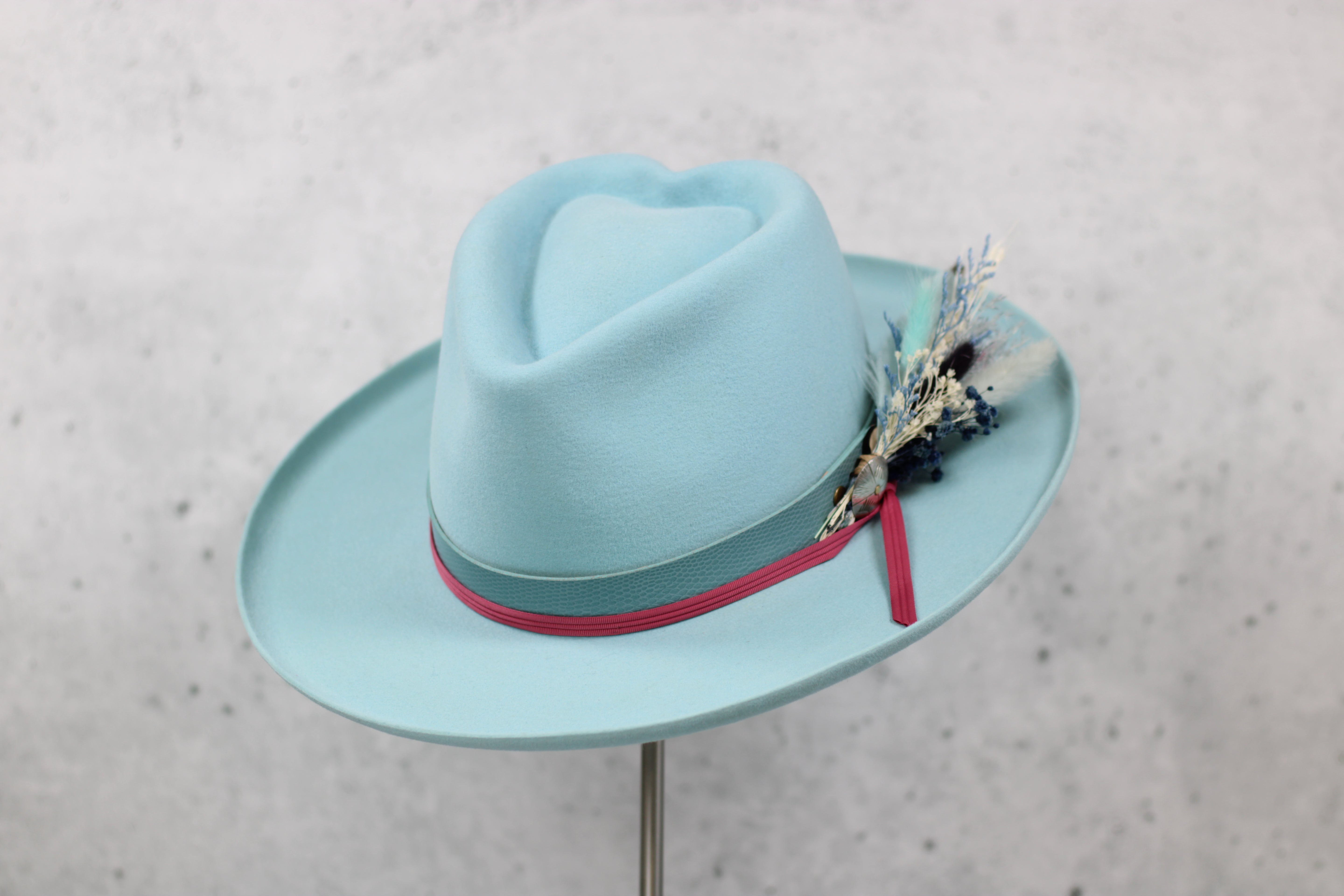 Light blue fedora hat with a pink and blue hatband and decorative feather 