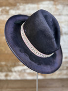 Side view of weathered violet-charcoal felt Gus hat with pencil curl brim, lilac petersham grosgrain ribbon, rhinestone band, hand stitching, and diamond brand mark.